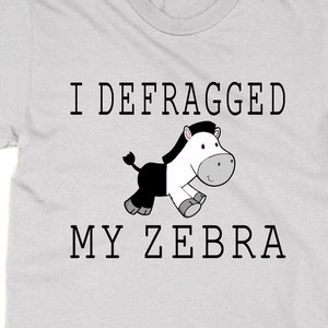 May include: A light grey t-shirt with black text that reads "I defragmented my zebra". A cartoon zebra is shown running to the right.