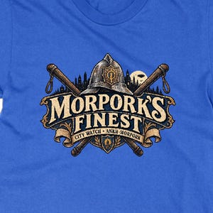 May include: A royal blue short-sleeved t-shirt featuring a graphic print of a helmet and two crossed batons. The text reads MORPORK'S FINEST CITY WATCH ANKH-MORPORK. The design includes a city skyline silhouette and a shield emblem in muted tones.