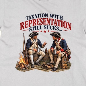 May include: A light grey t-shirt featuring a graphic of two colonial soldiers sitting on wooden crates by a campfire. The text above reads TAXATION WITH REPRESENTATION STILL SUCKS in blue and red lettering with three small red stars in the centre.