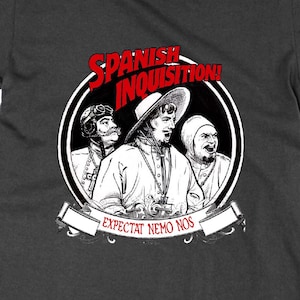 May include: Dark gray t-shirt featuring a black and white graphic of three figures with the text "Spanish Inquisition!" in red above them. Below the figures is a banner with the text "Expectat Nemo Nos".