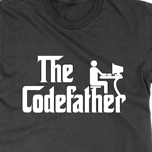 May include: A dark grey t-shirt with a white graphic design that says "The Codefather" with a stick figure sitting at a computer.