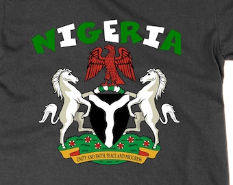 Puede incluir: Camiseta gris oscuro con la palabra "NIGERIA" en verde y blanco sobre un escudo de armas. El escudo de armas incluye un águila roja, dos caballos blancos y las palabras "UNITY AND FAITH, PEACE AND PROGRESS".