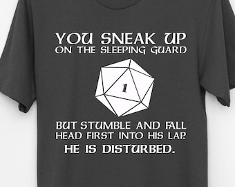 Puede incluir: Una camiseta gris oscuro con un gráfico blanco de un dado con un 1 en él. El texto en la camiseta dice "You sneak up on the sleeping guard, but stumble and fall head first into his lap. He is disturbed."