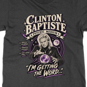 May include: A charcoal grey short-sleeve t-shirt featuring a graphic of Clinton Baptiste, a psychic medium, with a crystal ball. The text reads CLINTON BAPTISTE, PSYCHIC MEDIUM, PRIVATE READINGS, SPIRITUAL GUIDANCE, LOST LOVED ONES, and I'M GETTING THE WORD.
