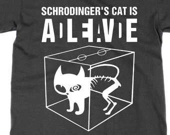 May include: Dark gray t-shirt with the text "Schrödinger's Cat Is Alive" in white. The graphic depicts a cat inside a box, with a skeleton visible. The cat's head and front legs are solid, while the rest is skeletal.