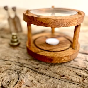 May include: A wooden incense burner with a glass dome and a small white candle inside. The burner is sitting on a rustic wooden surface.