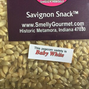 May include: A close-up of a bag of white popcorn kernels. The label reads "Savignon Snack&trade;" and "www.SmellyGourmet.com". A smaller label reads "This popcorn variety is Baby White".
