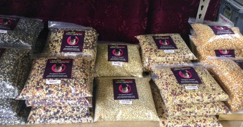 May include: Multiple bags of gourmet popping corn in various colors, including white, yellow, red, and black. The bags are labeled "Gourmet Popping Corn" and "Savory Snack".