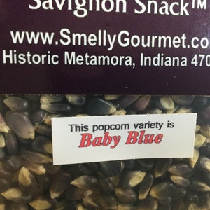 May include: Close-up of a bag of blue popcorn kernels. The label reads "This popcorn variety is Baby Blue".