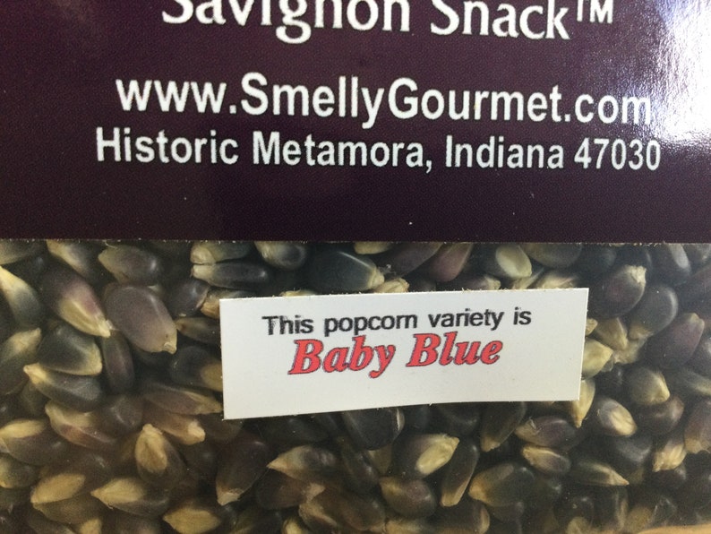 May include: Close-up of a bag of blue popcorn kernels. The label reads "This popcorn variety is Baby Blue".