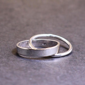 Könnte beinhalten: Zwei ineinandergreifende Ringe aus Silber, einer dicker als der andere, auf einem grauen Hintergrund.