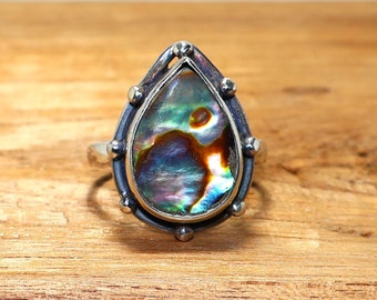 Könnte beinhalten: Ein silberner Ring mit einem Perlmutt-Abalone-Schmuckstein in Tropfenform.