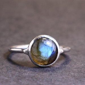 Puede incluir: Un anillo de plata con una piedra redonda de labradorita iridiscente.