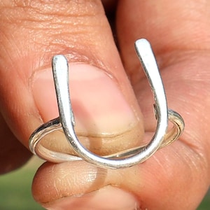 Puede incluir: Un anillo de plata con forma de U, usado en un dedo.
