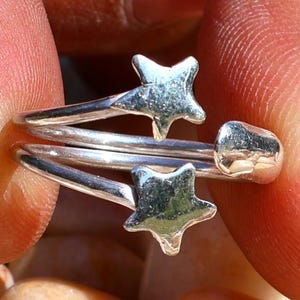 Könnte beinhalten: Ein silberner Ring mit drei sternförmigen Anhängern. Der Ring wird an einem Finger getragen.