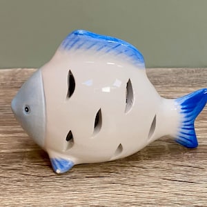 May include: White ceramic fish figurine with blue accents. The fish has cutouts on its body and a blue tail fin.