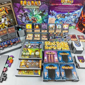 May include: A board game set with multiple boxes, cards, and game pieces. The boxes feature colorful illustrations of fantasy characters and the game's title, "Bruny!" in a stylized font. Various game components are organized in gray trays.