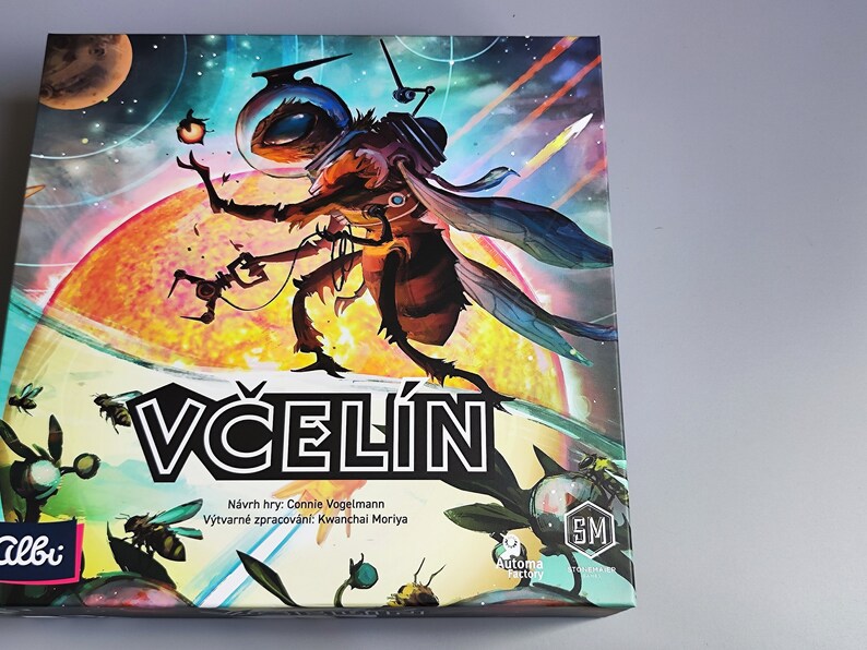 K&ouml;nnte beinhalten: Eine farbenfrohe Brettspielbox mit einer Biene, die einen Weltraumhelm tr&auml;gt und ein Werkzeug h&auml;lt. Die Box ist mit "VČELIN" betitelt und enth&auml;lt den Text "N&aacute;vrh hry: Connie Vogelmann" und "V&yacute;tvarn&eacute; zpracov&aacute;n&iacute;: Kwanchai Moriya".