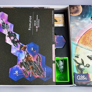 K&ouml;nnte beinhalten: Eine ge&ouml;ffnete Spielschachtel, die das Spielbrett, die Spielfiguren und die Anleitung zeigt. Das Spielbrett ist eine dunkelblaue und violette Weltraumszene mit einem Raumschiff und Planeten. Die Spielfiguren sind klein, gr&uuml;n und bienenf&ouml;rmig. Die Schachtel ist mit "Poppleton" und "Albi" beschriftet.