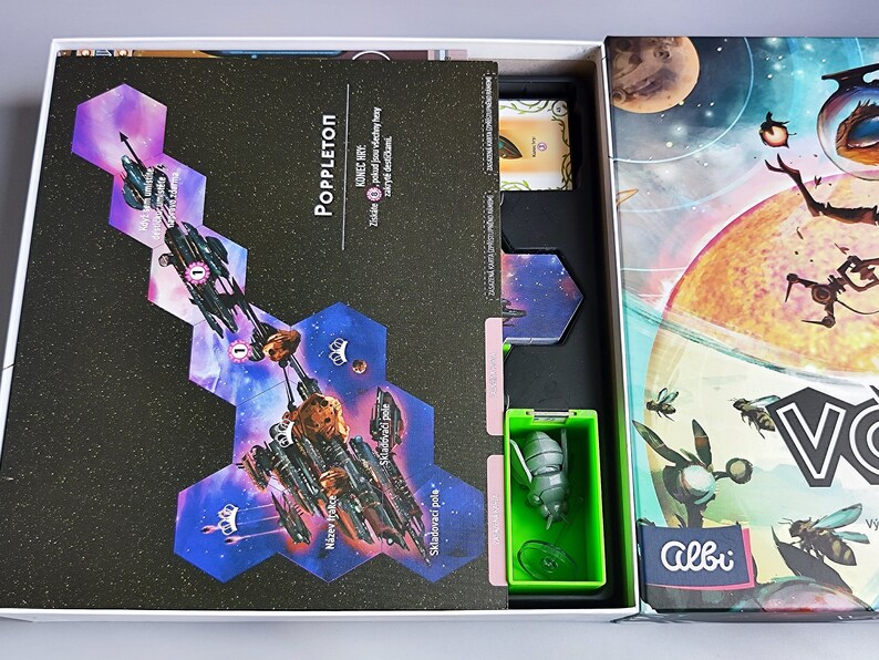 K&ouml;nnte beinhalten: Eine ge&ouml;ffnete Spielschachtel, die das Spielbrett, die Spielfiguren und die Anleitung zeigt. Das Spielbrett ist eine dunkelblaue und violette Weltraumszene mit einem Raumschiff und Planeten. Die Spielfiguren sind klein, gr&uuml;n und bienenf&ouml;rmig. Die Schachtel ist mit "Poppleton" und "Albi" beschriftet.