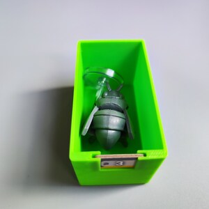 K&ouml;nnte beinhalten: Eine gr&uuml;ne Plastikbox mit einer grauen Insektenfigur im Inneren. Die Box hat die Nummer "3" auf der Vorderseite.