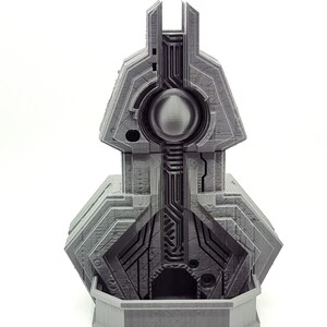 May include: A grey 3D printed model of a futuristic building with a circular opening in the centre. The building has a geometric design with intricate details.