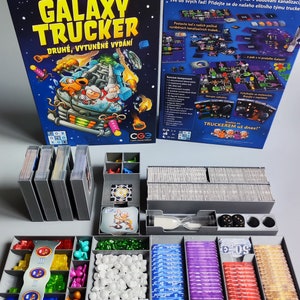 Könnte beinhalten: Ein Brettspiel namens "Galaxy Trucker" mit einer bunten Schachtel und Spielfiguren. Das Spiel geht darum, Raumschiffe zu bauen und darum, der beste Trucker der Galaxie zu werden.