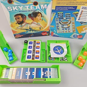 Pode incluir: Um jogo de tabuleiro verde e azul chamado Sky Team: Hladke Pristani. O jogo inclui um tabuleiro de jogo, cartas, dados e torres. O jogo consiste em pousar aviões com segurança.
