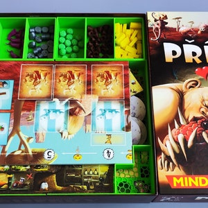 May include: A green and brown board game box with the title "Příšerky z Po". The box is open and shows the game components, including cards, tokens, and dice. The box art features a cartoon monster with a heart above its head.