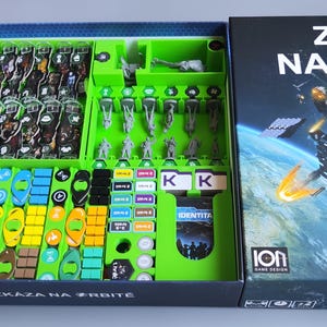 May include: A green and black board game organiser with compartments for storing game pieces. The organiser is labelled "Zkaza na Orbite".
