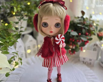 May include: A doll with blonde hair, wearing a red fur vest, earmuffs, and boots. The doll is holding a red and white swirled lollipop. The doll is wearing a red and white striped dress and red and white striped leggings.
