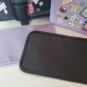 May include: A selection of small, decorative bags and accessories. The image shows a black bag with a flamingo patch, a light purple bag, and a black rectangular item. A light purple bag with decorative pins is also visible.