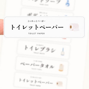 May include: A white rectangular label featuring the Japanese text for toilet paper, the English text TOILET PAPER, and a small illustration of a roll of toilet paper. The label is part of a larger sheet of vocabulary stickers for household items.