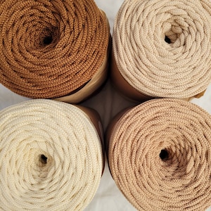 May include: Four spools of cotton rope in different shades of brown. The spools are arranged in a square pattern on a white surface.