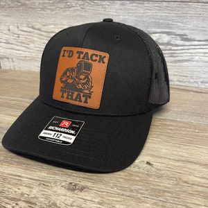 May include: Black trucker hat with a brown leather patch that says "I'd Tack That". The patch features a cartoon image of a welder. The hat is adjustable and has a Richardson 112 logo.