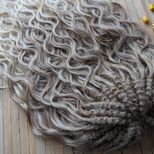 May include: A long, wavy, blonde and brown ombre wig with a braided base. The wig is styled in loose curls and has a natural, tousled look.