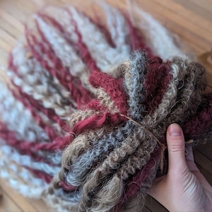 May include: A bundle of synthetic hair extensions in shades of burgundy, gray, and white. The hair is in a loose, wavy style.