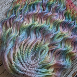 May include: A set of rainbow colored synthetic hair extensions. The hair is wavy and has a light pink, blue, green, and yellow color scheme.