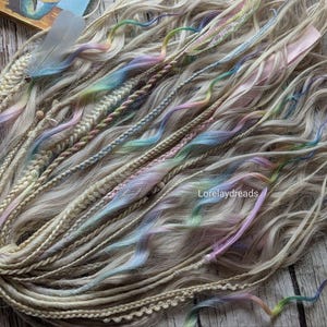 May include: A set of blonde synthetic hair extensions with colorful braids woven in. The braids are in shades of blue, pink, and green. The hair is long and wavy.