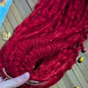 May include: A bundle of bright red synthetic dreadlock hair extensions. The hair is tied together with a brown string.