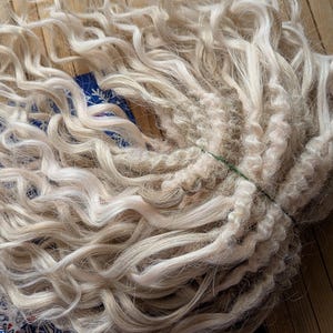 May include: A bundle of long, blonde, curly hair extensions. The hair is tied together with a green rubber band.