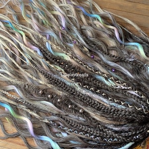 Peut inclure: Un ensemble d'extensions de cheveux synthétiques brunes, blondes et blanches avec des accents bleus, verts et violets. Les extensions sont tressées et comportent des perles et d'autres éléments décoratifs.