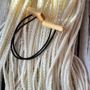 Op de afbeelding: Een close-up van een bundel witte garen vlechten met een houten haarspeld en een zwart elastiek.