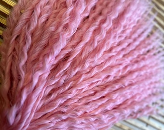 Op de afbeelding: Een bundel roze synthetische haarverlengingen met een krullende textuur. Het haar is bij elkaar gebonden met een elastiekje.