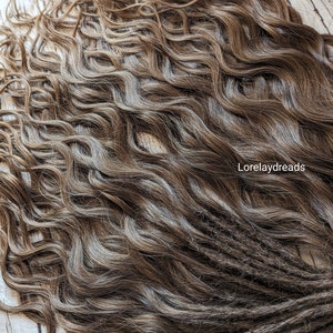 May include: A set of brown and blonde wavy synthetic dreadlocks. The dreadlocks are tied together with a blue string.