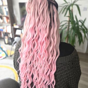 May include: Long, wavy pink hair extensions with a dark root and a gradient effect. The hair is styled in a ponytail, with the ends of the hair a vibrant pink color. The hair extensions are a popular choice for adding length and volume.