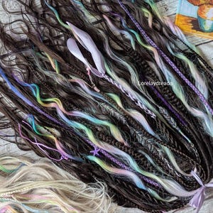 May include: A collection of brown, white, and multi-colored synthetic dreadlocks. The dreadlocks are arranged in a loose bundle and have a variety of textures and colors, including light blue, green, pink, and purple.