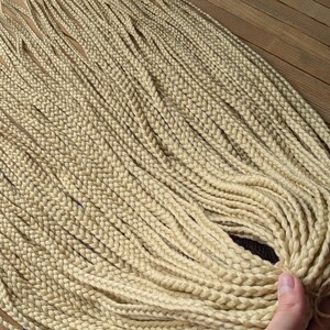 Peut inclure: Un grand paquet de cheveux synthétiques pour tresser de couleur blonde claire. Les cheveux sont en longues tresses épaisses.