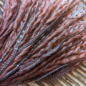May include: A bundle of brown and blonde synthetic hair extensions with white beads woven in. The hair is curly and textured.