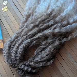 May include: A set of long, curly hair extensions with a brown to light gray ombre color. The hair is arranged in a loose bundle.